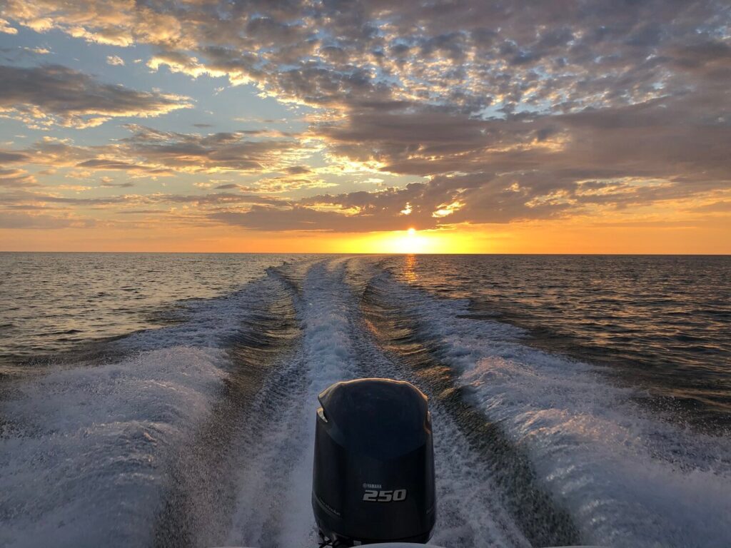boat driving in the open ocean with sunset in the background