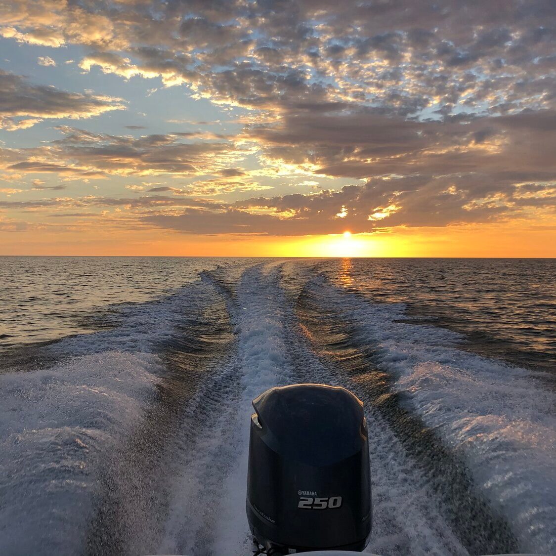 boat driving in the open ocean with sunset in the background